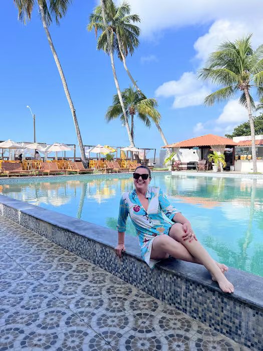 Mulher à beira da piscina de uma pousada, cercada de coqueiros